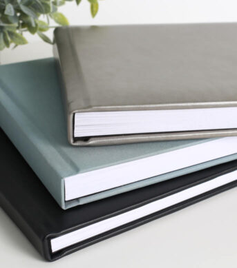 Stacked photo albums with linen and leather covers in gray, teal, and black.