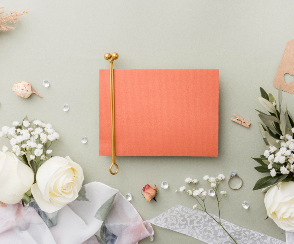 A wedding guest book placed on a table, surrounded by floral arrangements and a ring, with a sign inviting guests to sign.