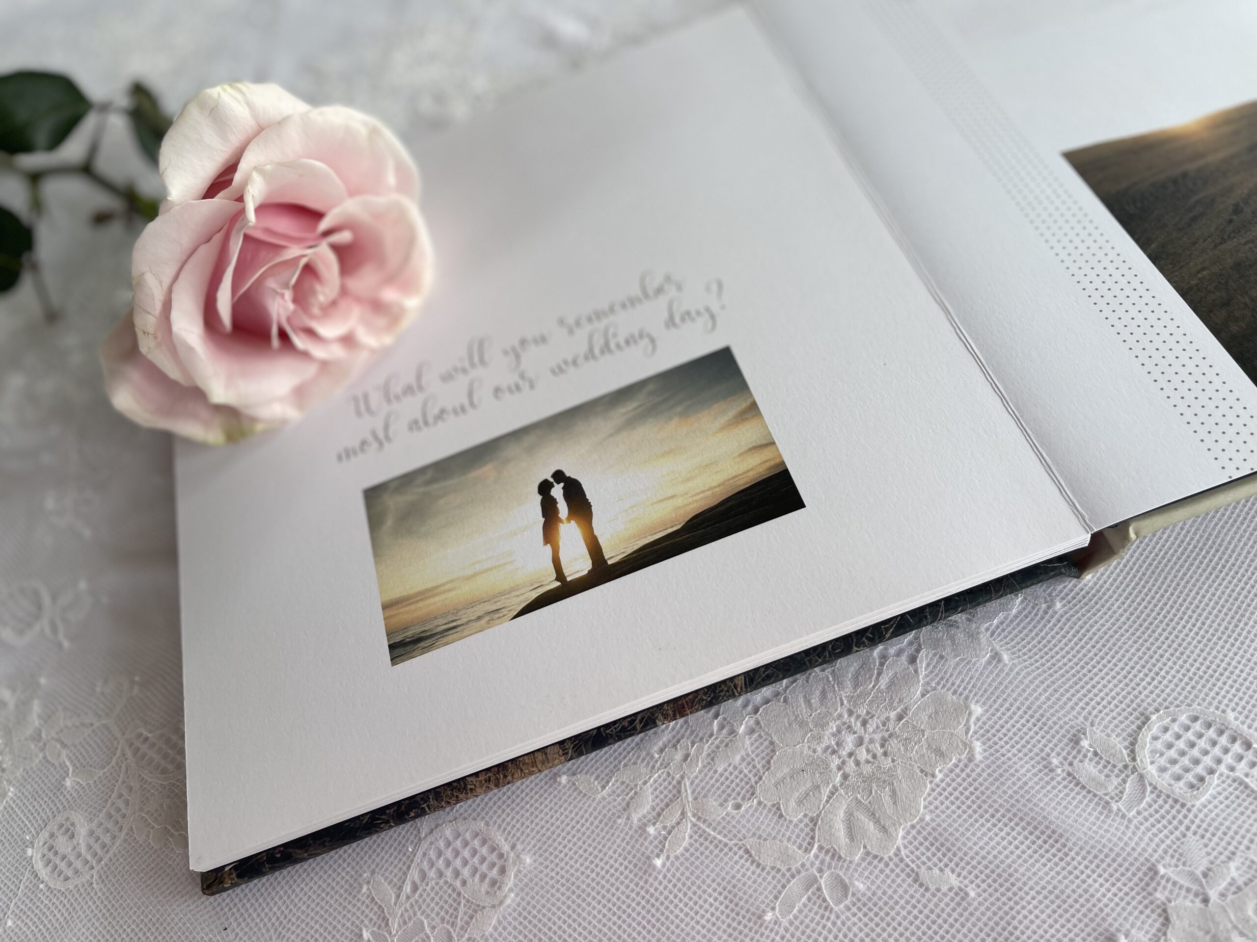 Wedding album with a photo of a bride and groom silhouette at sunset, accompanied by a pink rose and text "Will you remember? Most about our wedding day?" on lace.